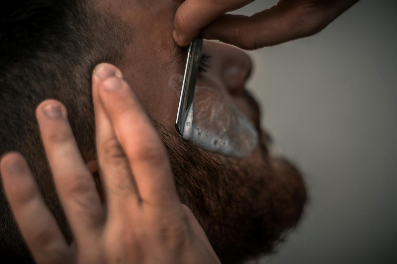 Image détaillée en gros plan d'un coiffeur utilisant un rasoir pour une coupe précise de la barbe dans le salon de coiffure.