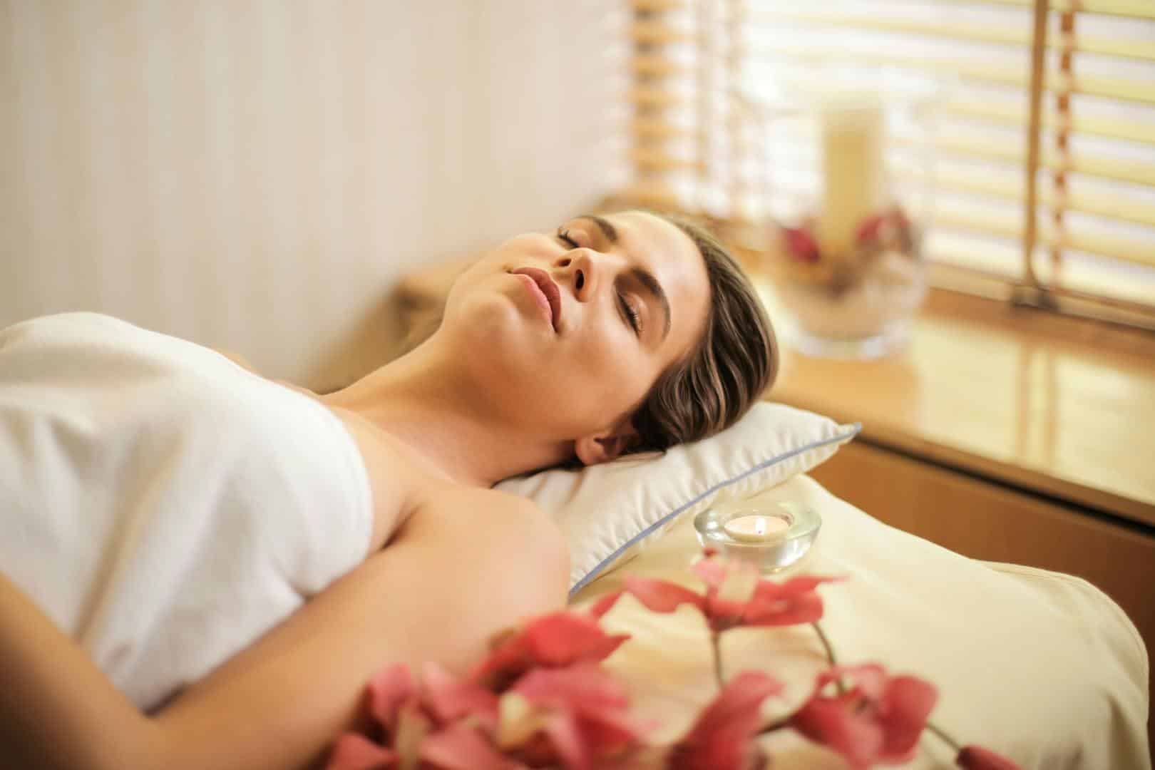 Femme bénéficiant d'une journée de détente au spa avec des fleurs et des bougies à l'intérieur.