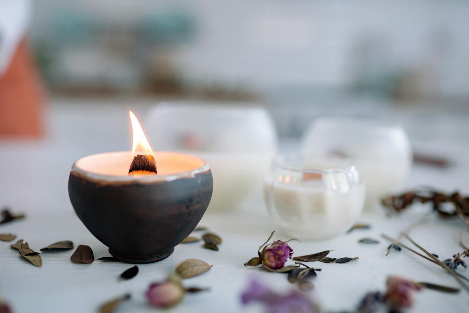 Flamme de bougie chaude dans un support en céramique avec fleurs séchées sur table.