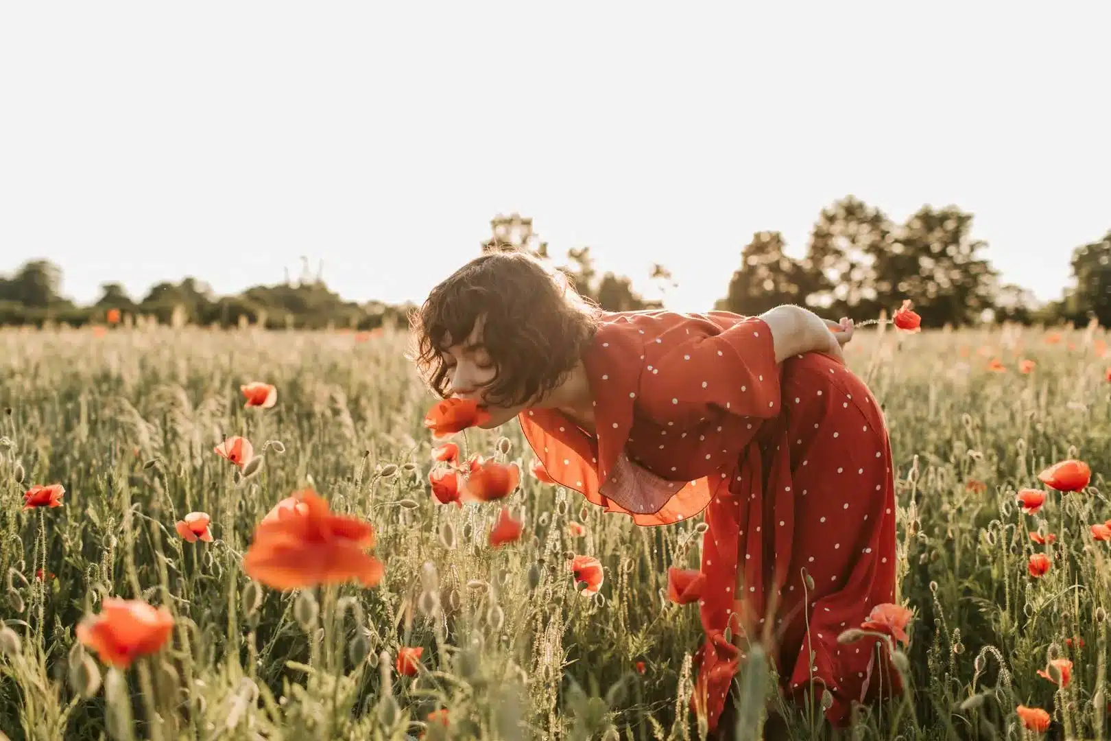 Une femme en robe rouge profite du parfum des fleurs dans un champs de coquelicots